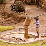 A boy holding onto a water pump