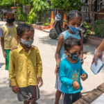 Children wearing masks wait in line for food