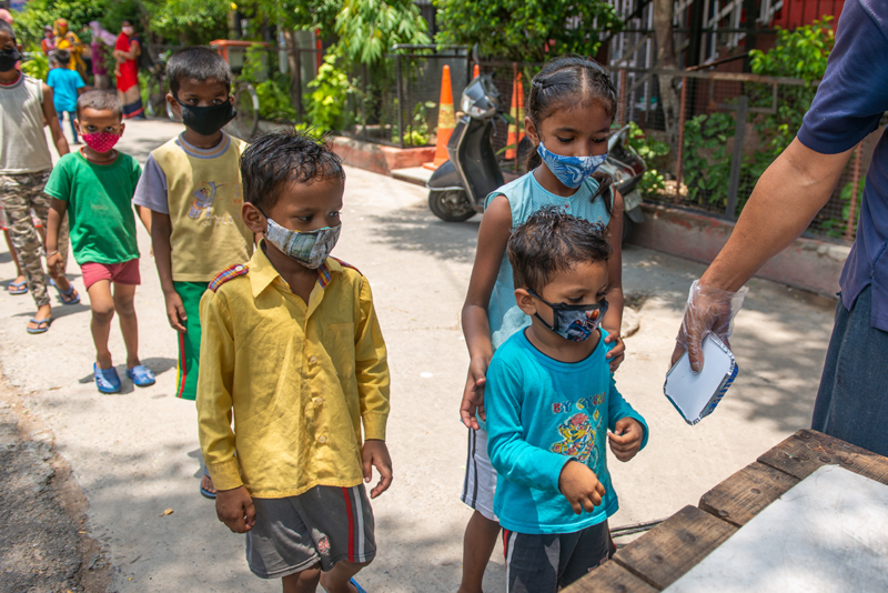 Children wearing masks wait in line for food