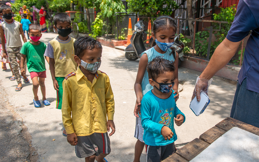 Children wearing masks wait in line for food