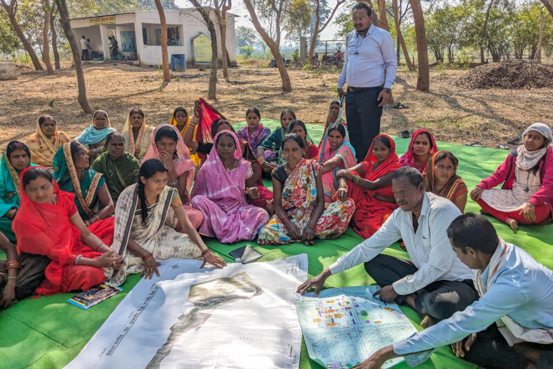 Researchers and female farmers sit on a green tarp during a focus group discussion.
