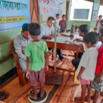 A doctor weighing a child on a scale as more children wait their turn